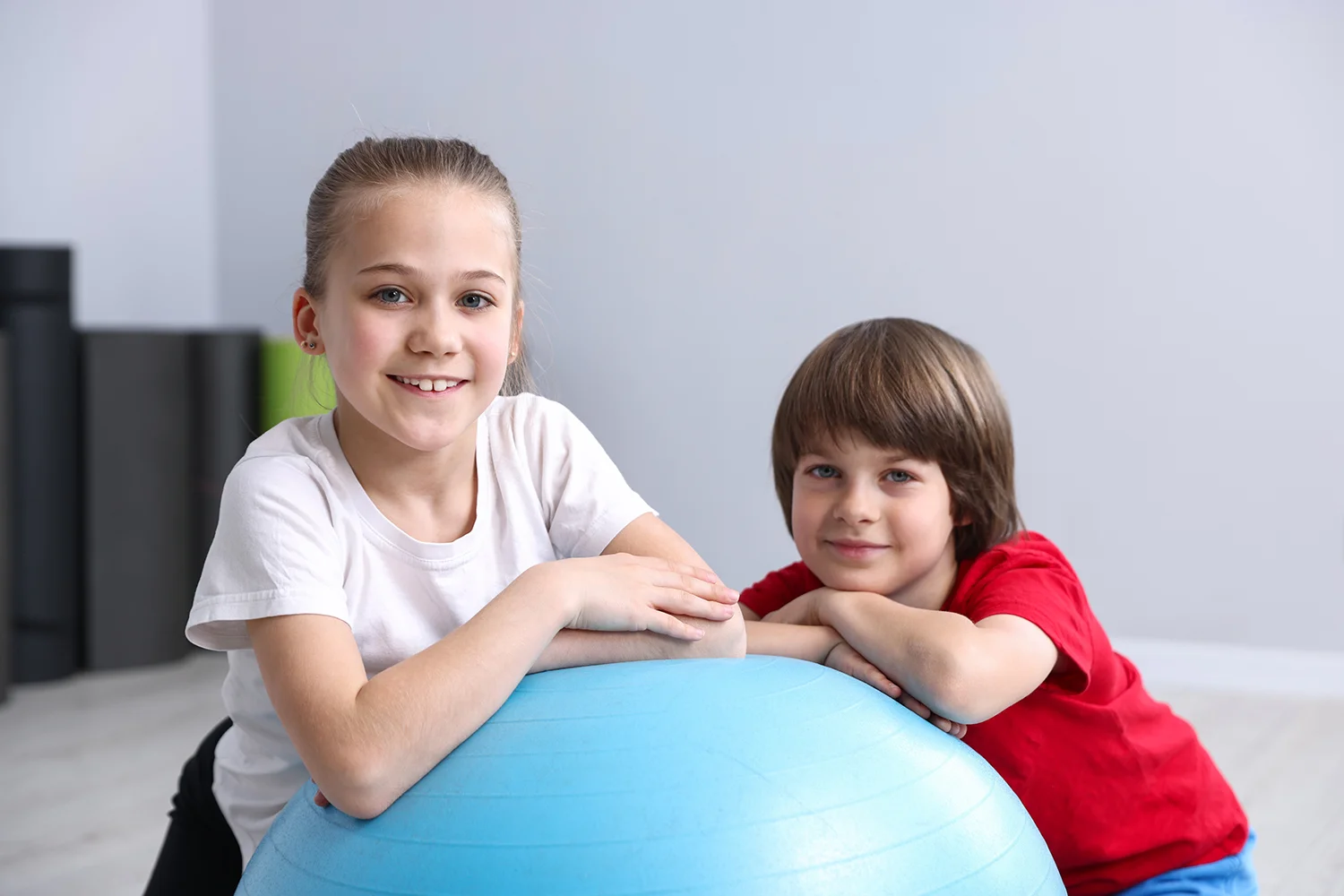 two happy children posing with a blue fitness ball